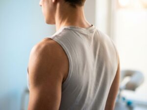 Gezonde, ontspannen schouders en bovenrug van achteren, persoon draagt sportkleding in natuurlijk licht