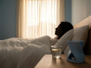 Persoon slaapt vredig op witte kussens met warm licht door gordijnen, glas water op nachtkastje voor gezonde slaap