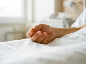 Hand rustend op wit klinisch oppervlak met licht gekrulde vingers, suggestief voor gevoelloosheid, orthopedische kliniek op achtergrond.